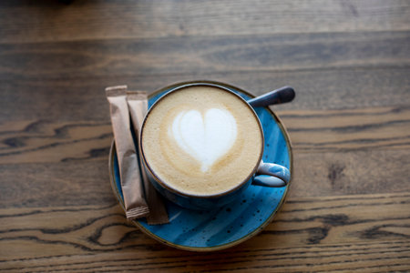 blue cup with coffee with heart-shaped froth on the table with a bag of sugar cup,