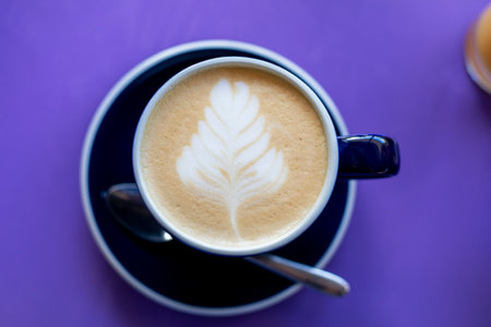 Cup of latte coffee with a drawn leaf on a purple table, horizontalの写真素材