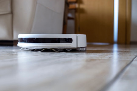 white robot vacuum cleaner cleans wool in a room on the floor near the sofa in a bright interior,の写真素材