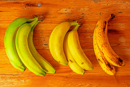 three bunches of bananas from green to overripe on a wooden backgroundの写真素材