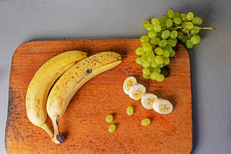 bunch of bananas with a bunch of green grapes on a wooden cutting board on a gray background. flatlayの写真素材