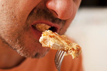 man taking a bite of a piece of fried chicken meat from a fork. dinnerの写真素材