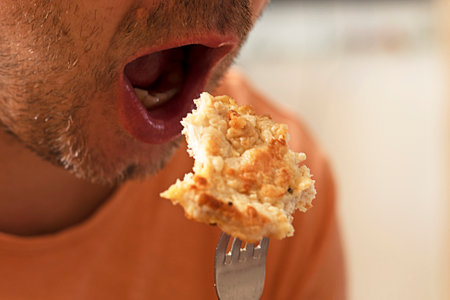 man taking a bite of a piece of fried chicken meat from a fork.の写真素材
