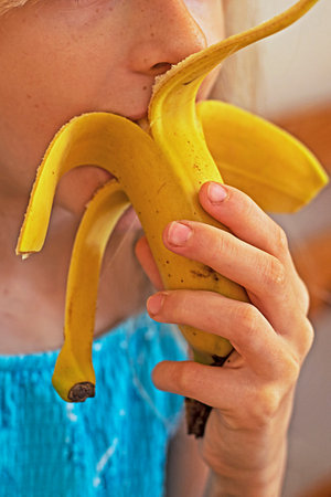 girl with long hair happily eats a sweet banana at homeの写真素材