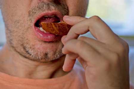 man puts a piece of cheese sandwich into his mouthの写真素材