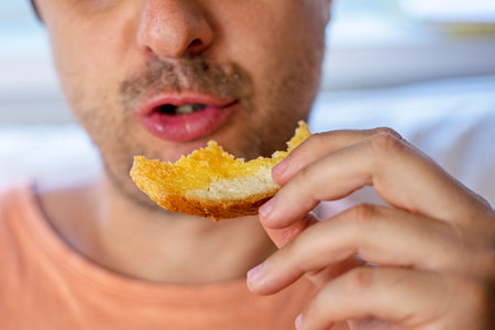 close-up of a man holding a cheese sandwich in his hands in front of his mouthの写真素材