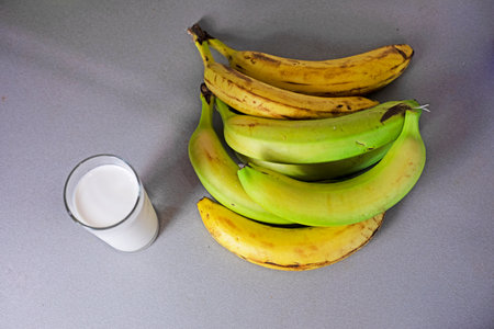 glass of banana milk next to a bunch of bananasの写真素材