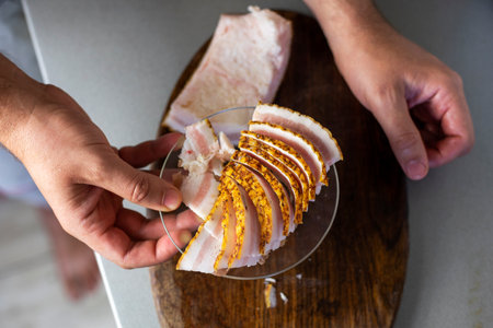Use your hand to pick up thin pieces of chopped bacon on a cutting board and place on a plate. flatlayの写真素材