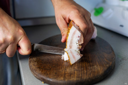man cuts a piece of bacon into thin pieces with a knife on a cutting board