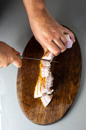man cuts a piece of bacon into thin pieces with a knife on an oak cutting board. flatlayの写真素材