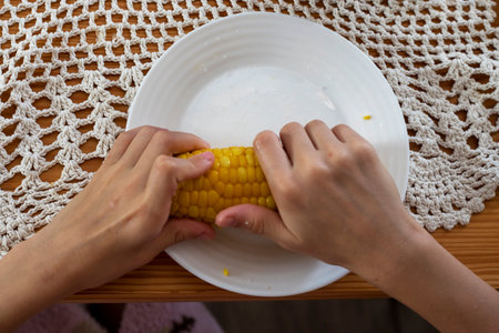 girl spreads butter and salt with her hands on a head of sweet cornの写真素材