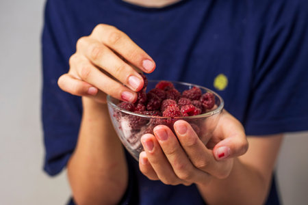 hands hold a glass bowl with raspberries and take berries from it