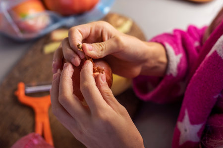 children's hands hold an onion and peel the skin in the kitchen before cookingの写真素材
