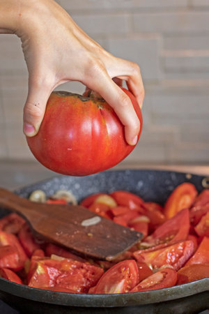 girl holds a pink tomato with her hand over a frying pan. flatlayの写真素材