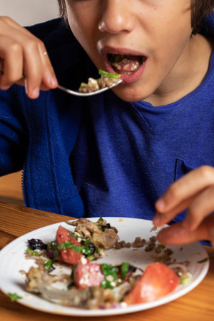 boy eats buckwheat porridge with vegetable salad and meat with a forkの写真素材