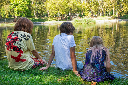 children schoolchildren sitting with their backs near the lakeの写真素材