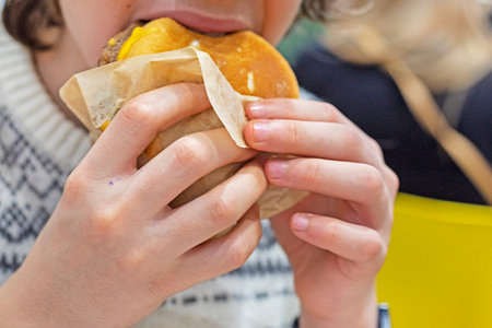 teenager bites off a fresh hamburger while holding it in his hands. snack. street food