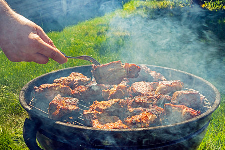 man cooking meat on the grill on a barbecue on a sunny day.Holiday Family weekends and restの写真素材