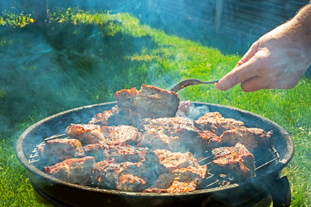 man cooking meat on the grill on a barbecue on a sunny day.Holiday Family weekends and restの写真素材
