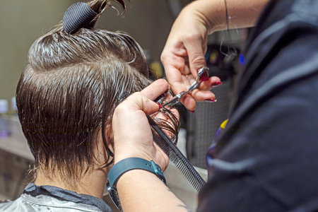 barber cuts the hair near the ears of a teenager with scissors in a beauty salon. Personal styleの写真素材