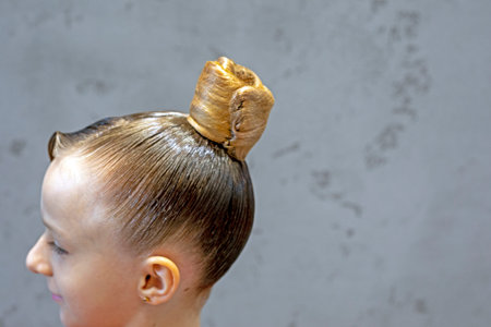 Hairstyle slicked back with a high bun in a net for a girl on a gray background