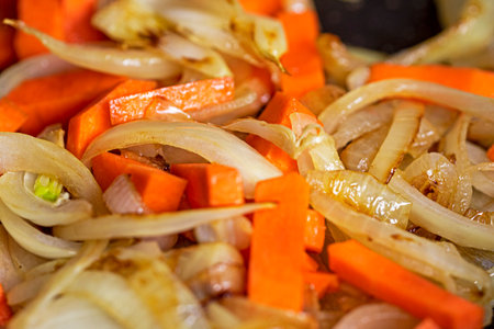frying half rings of onion with pieces of fresh carrot in a saucepan. Vegetarian nutrition and healthの写真素材