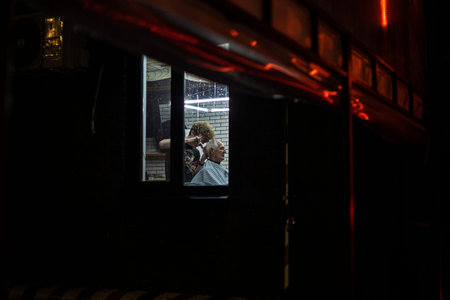 barbeshopper creates hairstyle for elderly man. view through window in eveningの写真素材