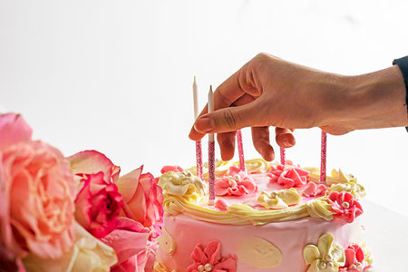Insert pink sparkling candles into a festive mousse cake in pink and white shades with pink roses.