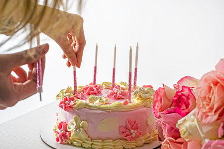 Insert pink sparkling candles into a festive mousse cake in pink and white shades with pink roses.の写真素材