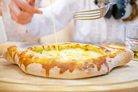 Eating Adzharian khachapuri with a fork on a wooden board on the table