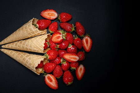 Fresh ripe strawberries are spilling out of the three waffle cones on dark background in minimalist style. Fresh organic berries, perfect for healthy eating.の写真素材