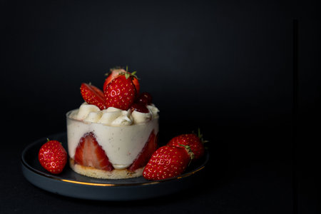 Strawberry mousse dessert topped with fresh strawberries on dark plate.