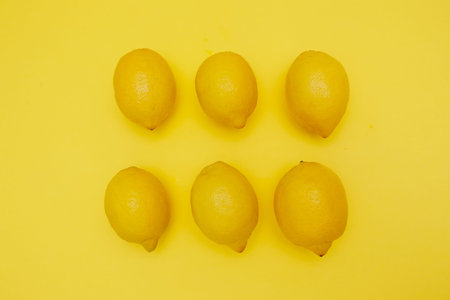 Minimalistic flat lay composition of six fresh lemons arranged in two neat rows of three on vibrant...