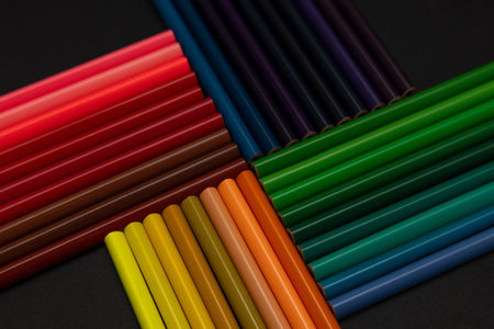 Close-up colorful pencils arranged in geometric cross shape on black background. Creative flat lay...