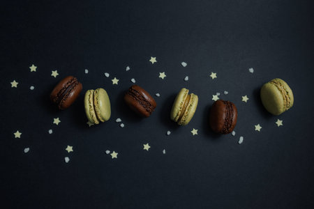 Creative flat lay of six chocolate and pistachio French macarons arranged in a curved line on a dark...