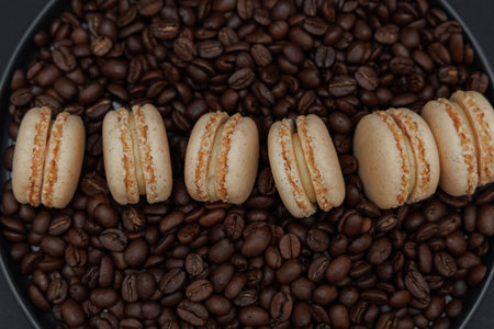 Elegant composition of six vanilla French macarons placed on a dark plate with coffee beans on black background. Minimal dessert still life with rich tones and stylish food photography.の写真素材
