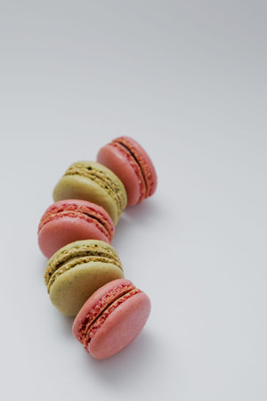 Five green and pink French macarons arranged in a gentle arc on a clean white background. Colorful...