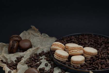 Elegant composition of vanilla French macarons arranged on a dark plate with coffee beans and baking paper on a dark background.の写真素材