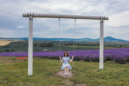 Young beautiful woman is sitting on a swing in a lavender fieldの写真素材
