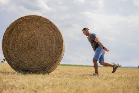 A man pushes a stack of hay in a fieldの写真素材