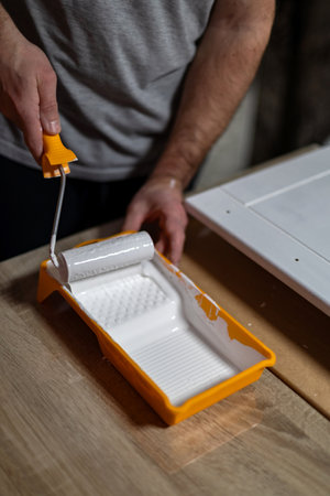Person painting a door with a roller and tray in a home renovation project during the afternoonの写真素材