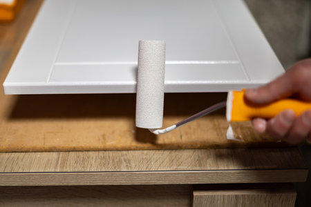 Home improvement project with paint roller applying white paint to cabinet door in workshopの写真素材