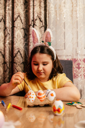 Child decorating Easter eggs at home during springtime celebrations with colorful craft supplies on the tableの写真素材