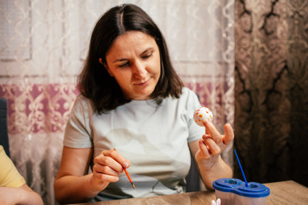 Woman decorating an egg with vibrant colors during a festive activity at homeの写真素材