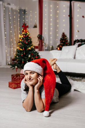 Woman in Santa hat enjoying holiday decorations in a cozy living room with Christmas trees and giftsの写真素材