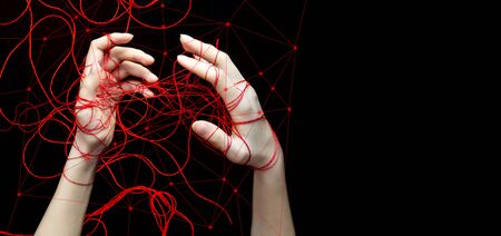 The concept of social networks, social dependence. Two of the womens hands were entangled in a net of red threads. Black isolated background, copy space, banner, selective focusの写真素材