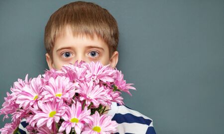 A young teenager in a striped t-shirt looks out from behind a bouquet of beautiful chrysanthemums that he holds in his hands. Isolated grey background, greeting card for grandmas Day, womens day.の写真素材
