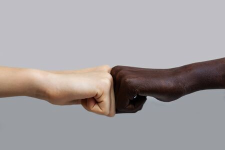 The black African-American hand and the white European hand give a blow to the partnership and cooperation agreement against a grey isolated background.The concept of combating racismの写真素材