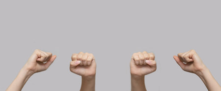 White human hands with raised fists in the air on a gray isolated background. Close-up, banner, copy...
