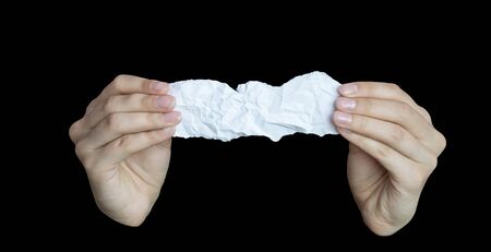 Female hands hold a piece of white crumpled paper on a black isolated background. Close-up, space for text and layout, space for copying.の写真素材
